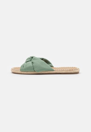 Sandale plate avec semelle en jute tressée et large bride en tissu vert sauge torsadée sur le dessus du pied, conçue pour un usage décontracté.