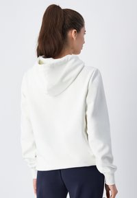 Sudadera blanca hecha de material suave, con un bolsillo canguro, puños acanalados y capucha con cordón. Textura suave, corte estándar.