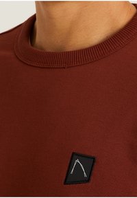 Felpa bordeaux con collo a costine, caratterizzata da una patch rettangolare nera con un logo bianco di una montagna sul petto.