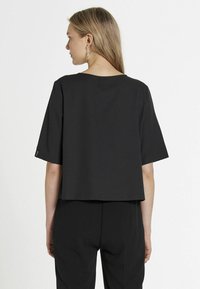 T-shirt nera cropped realizzata in morbido cotone, con scollatura ampia e maniche corte, caratterizzata da cuciture minime e una vestibilità rilassata.