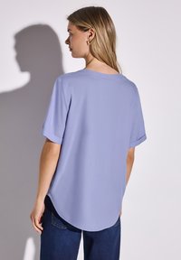 Blusa lilla con maniche corte, scollatura rotonda e orlo curvo. Realizzata in un materiale morbido, con una vestibilità comoda e polsini delle maniche arrotolati.