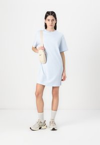 Svetlo modra majica obleka s kratkimi rokavi, izdelana iz mehke tkanine. V kombinaciji z bež Nike čez ramensko torbico in športnimi copati z večbarvnim podplatom.
