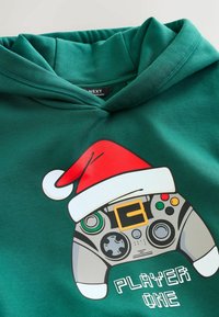 Green hoodie featuring a graphic of a game controller topped with a red Christmas hat and the text "PLAYER ONE" in white. Soft fabric texture.