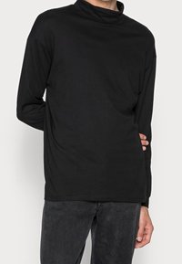 Czarna, długosleeve'owa koszulka z golfem wykonana z miękkiego materiału, o luźnym kroju i minimalnych detalach szwów. Noszona z ciemnymi spodniami.