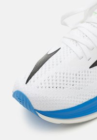 Scarpa sportiva bianca con parte superiore in rete traspirante, dettagli neri e suola blu. Presenta lacci prominenti e parte superiore testurizzata per una migliore aderenza.