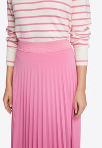 Falda plisada rosa con una cinturilla de textura y elástica y una suave combinación de tonos rosas, combinada con una blusa de manga larga a rayas en color crema y rosa.