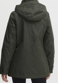 Osoba v tmavě zelené bundě s kapucí, zobrazená zezadu, s knoflíkovými manžetami a dlouhými rukávy.