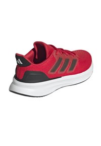Zapatilla deportiva roja con parte superior texturizada, tres rayas negras y una media suela blanca. El contrafuerte negro en el talón añade estabilidad.