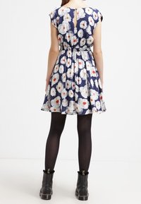 Abito floreale con maniche corte, sfondo blu navy, fiori bianchi e rossi, vita aderente, gonna svasata e dettagli a forma di chiave sul retro.