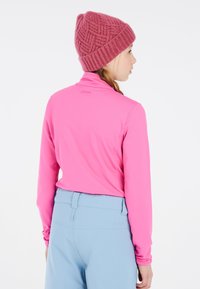 Top de manga larga rosa con cuello alto, combinado con pantalones azul claro. El sombrero es un tejido de punto texturizado de color rosa intenso con borde enrollado.