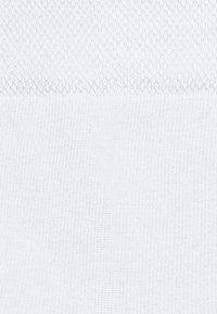 Biała teksturowana tkanina z dwoma różnymi wzorami dzianinowymi, jednym na górze z wzorem diamentowym i gładką dzianiną poniżej.