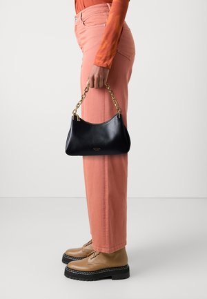 Black leather handbag with gold-tone chain handle, curved shape, and gold foil logo. Paired with pink pants and brown lace-up shoes.