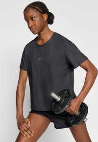 Μαύρο αθλητικό μπλουζάκι με υφασματικό μοτίβο, στρογγυλή λαιμόκοψη και κοντά μανίκια, σε συνδυασμό με μαύρο σορτς και βαρυμένο αλτήρα.