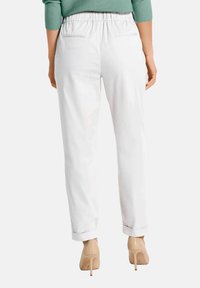 Witte, elastische taillebroek met oprolmanchetten en achterzakken, van textuurstof, gecombineerd met naakte hoge hakken.