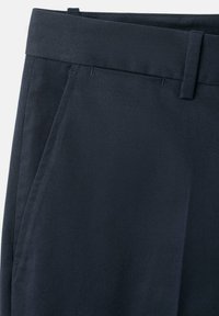 Pantalon bleu marine ajusté avec poches latérales, passants pour ceinture et taille, présenté sur un fond blanc.