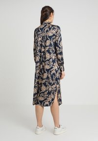 Marinblå klänning med ljusbeige bladmotiv, långa ärmar, knäppning vid kragen, medellång med sidofickor, stylad med vita sneakers.