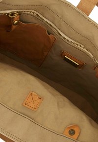 Interior de bolsa de lona en beige con detalles de cuero marrón. Cuenta con un bolsillo con cremallera y varios compartimentos interiores con detalles de costura.