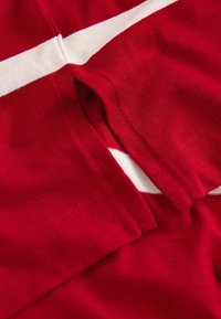 Roter Baumwollstoff mit weißen horizontalen Streifen, locker geschnitten und mit sichtbaren Stichdetails an den Kanten und Nähten.