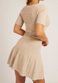 Abito beige a coste con top aderente e gonna svasata. Le maniche corte e un tessuto testurizzato con righe verticali esaltano il suo design.
