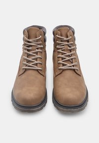 Stivali alla caviglia in pelle marrone con superficie texturizzata, punta rotonda, linguetta grigia a contrasto e lacci metallici. Suola in gomma con battistrada per una buona aderenza.