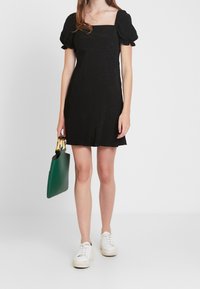 Musta mekko lyhyillä puffihaalareilla, neliönmuotoinen pääntie ja hienovarainen tekstuuri. Yhdistetty vihreään käsilaukkuun ja valkoisiin tennareihin.