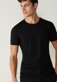 Schwarzes Rundhals-T-Shirt aus weichem Baumwollstoff. Kurze Ärmel, schlanker Schnitt und glatte Textur. Keine sichtbaren Muster oder Grafiken.