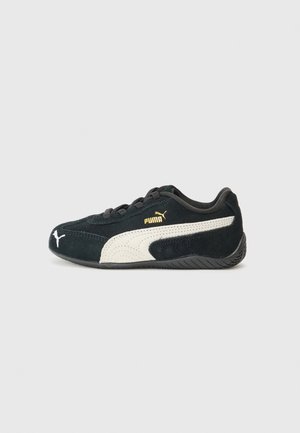 Baskets Puma noires avec bande blanche et logo, semelle basse profil et lacets, vues de profil gauche sur fond clair.