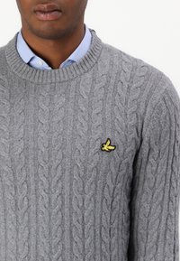 Suéter gris de punto con un cuello redondo acanalado y un pequeño logo de un pájaro amarillo en el lado izquierdo del pecho. Material de lana texturizada.