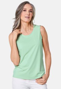 Lichtgroene mouwloze top van zachte stof, met een ronde halslijn en een relaxte pasvorm, gecombineerd met witte broeken.