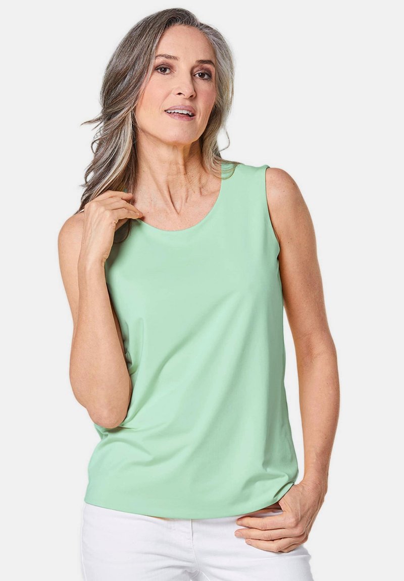 Lichtgroene mouwloze top van zachte stof, met een ronde halslijn en een relaxte pasvorm, gecombineerd met witte broeken.