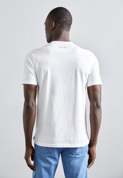 Valge puuvillane T-särk lühikeste varrukatega, ümar kaelus ja väike logo taga. Ühendatud siniste teksadega, millel on nähtav õmblus.