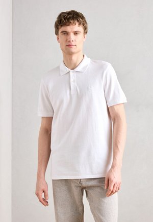 Polo blanc en coton avec manches courtes, patte de boutonnage à deux boutons et logo brodé subtil. Associé à un jean en denim de couleur claire.