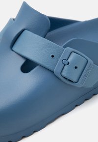 Blauwe rubberen sandaal met een gestructureerd oppervlak, voorzien van een verstelbare gesp en een gevormde voetbed. Gemoed sole met een laag profiel.