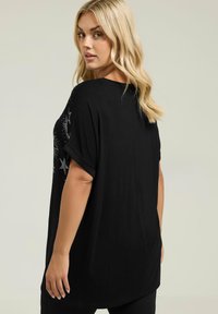 Czarna tunika z krótkim rękawem, zdobiona srebrnymi gwiazdkami z jednej strony, w luźnym kroju, z miękkiego materiału bawełnianego, sięgająca bioder.