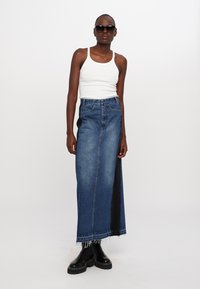 Denim maxiszoknya elöl résnyitással, kék mosással, rojtos szegéllyel, fehér toppal és fekete, vastag talpú csizmával párosítva. Kiegészítve napszemüveggel.