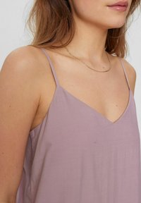 Top senza maniche lavanda con design a V, realizzato in tessuto morbido. Spalline sottili e vestibilità comoda per un maggiore comfort. Accento di collana a catena.