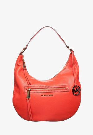 Sac à main Michael Kors en cuir rouge avec une forme arrondie, une poche frontale zippée, des accessoires dorés et un pendentif rond avec le logo MK suspendu à la bandoulière.