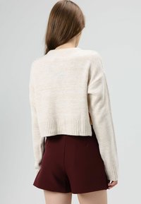 Beige cropped sweater with a ribbed hem and long sleeves, paired with burgundy shorts. Textured knit fabric with a subtle pattern.