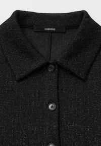Maglietta nera in maglia con una finitura texture, dotata di colletto e tre bottoni neri. L'etichetta riporta "someday". Leggeri riflessi argentati sparsi qua e là.