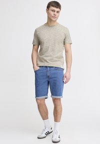 Beigen värinen harmaa lyhythihainen paita, siniset farkkushortsit käännetyllä helmalla, valkoiset joustavat sukat ja mustat sekä harmaat lenkkitossut.