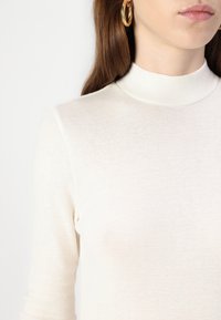 Maglione a collo alto color crema con un design aderente e maniche lunghe, realizzato in un tessuto morbido e leggero. Presenta una texture liscia.