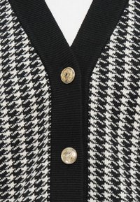 Black and white houndstooth patterned cardigan with black ribbed edges and two decorative gold buttons down the front.