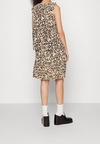 Robe à imprimé léopard beige avec des manches volantes, une jupe superposée et un tissu texturé. Portée avec des chaussures à plateforme noires et des chaussettes blanches.