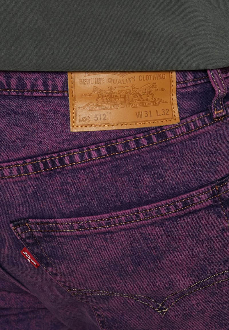Jeans de mezclilla morados con una etiqueta de cuero que muestra "Lote 512", W31 L32, y detalles en hilo dorado en los bolsillos y costuras.