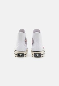 Hvite lerrets høye sneakers med rund lapp, svarte gummisåler og kontraststingdetaljer. Har et klassisk design og enkel form.