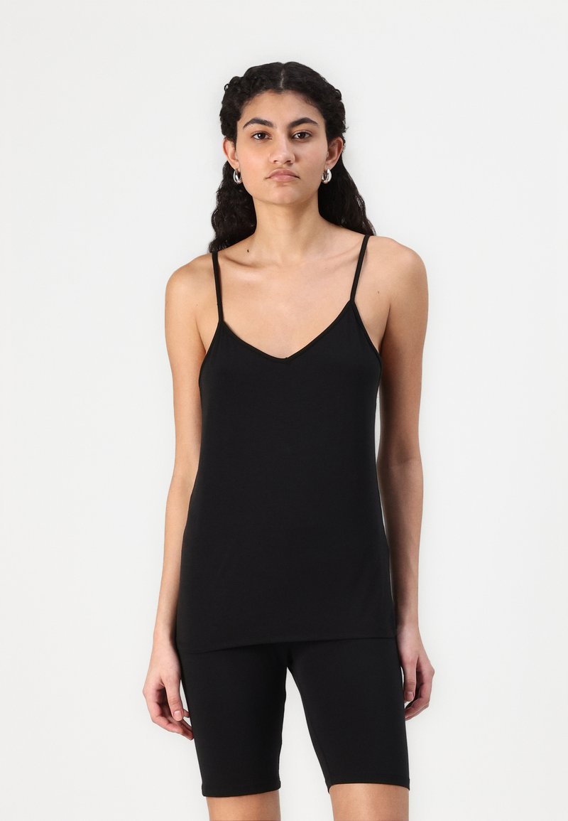 Canotta nera senza maniche con spalline regolabili, design a V, tessuto morbido, abbinata a pantaloni corti neri fino al ginocchio. Silhouette semplice e aderente.