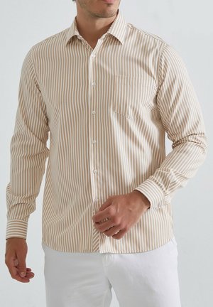 Chemise à boutons avec des rayures verticales beiges et blanches, à manches longues, poche poitrine et col classique. Fabriquée en tissu léger.