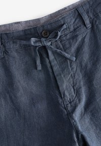 Pantaloni shorts in lino blu scuro con vita regolabile, chiusura con bottone e superficie testurizzata. Sono visibili cuciture di dettaglio lungo le cuciture.