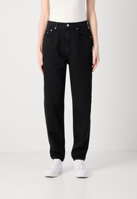 Mustat farkut suoranlahkeisella suunnittelulla, joissa on etutaskut, nappisuljenta ja valkoiset tennarit. Kangas näyttää vankalta.