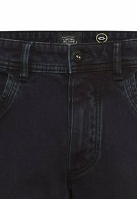 Donkerblauwe denim jeans met een frontale knoopsluiting, riemlussen en een standaard vijfzakdesign. De stof heeft een gladde en iets glanzende textuur.